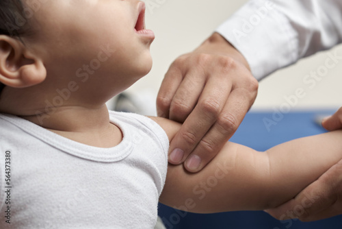 unrecognizable physician's hands palpating humeral brachial pulse in infant patient photo