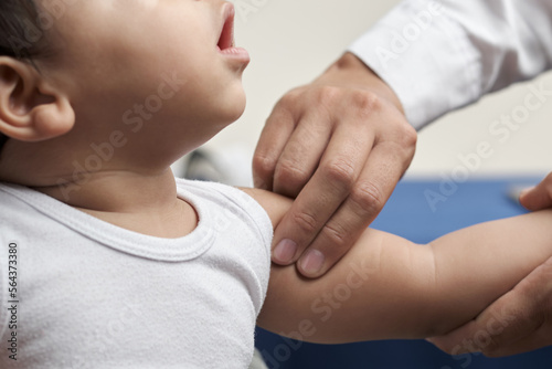 unrecognizable physician's hands palpating humeral brachial pulse in infant patient