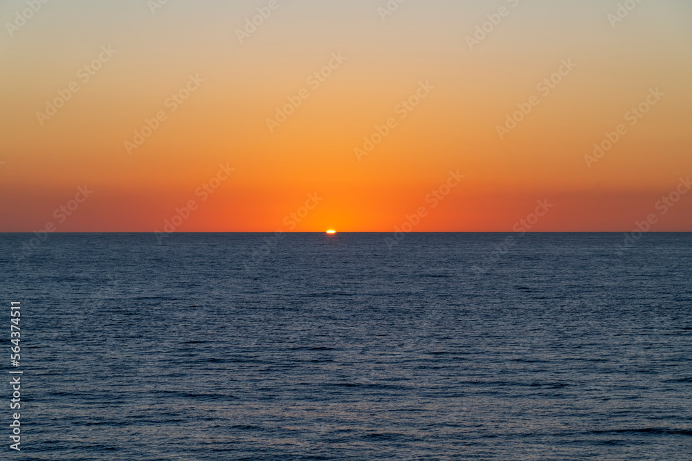 Just a sliver of sun remains under a colorful orange sky at sunset at the port of Cabo San Lucas, Mexico.