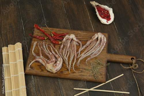 raw squid tentacles with pepper, salt, Japanese sticks on kitchen board ready for cooking closeup photo