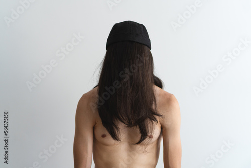 Young, athletic shirtless man with his face covered by his own hair wearing a brimless cap with a white background. Artistic photo. photo