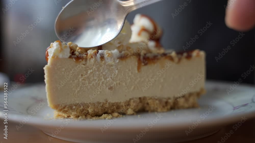 Close up of a spoon scooping through a piece of pasty made of mascarpone cream with topping of nuts and caramel.