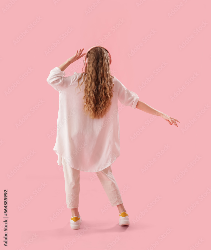 Young woman in headphones dancing on pink background, back view Young woman in headphones dancing on pink background, back view
