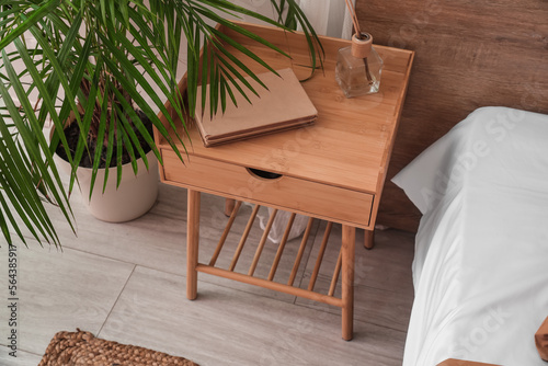 Wooden bedside table with books and reed diffuser in bedroom