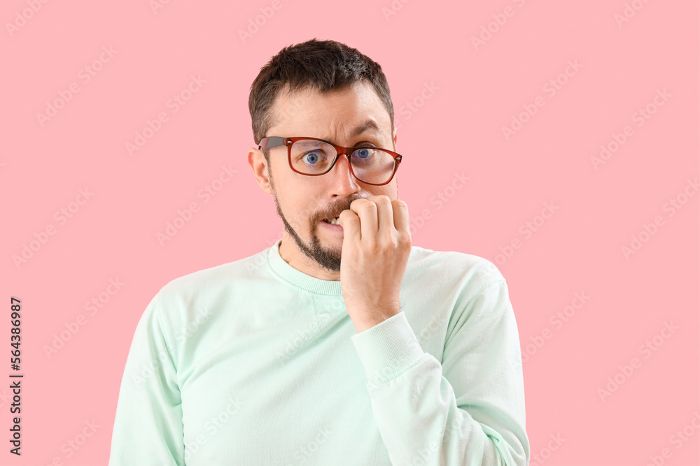 Handsome man in eyeglasses biting nails on pink background Handsome man in eyeglasses biting nails on pink background