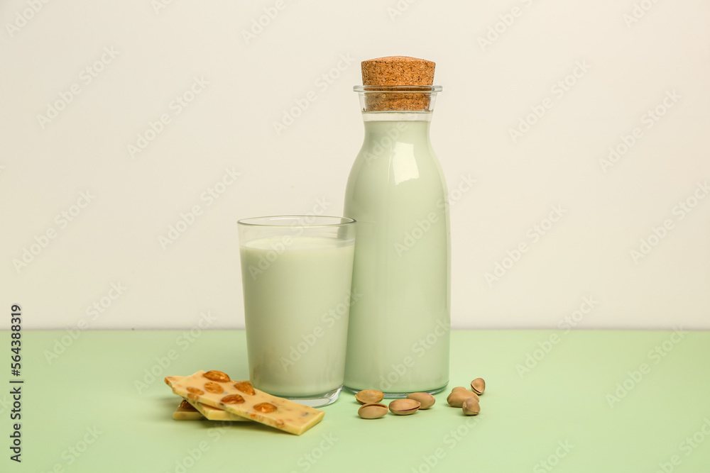 Glass and bottle of delicious pistachio milk and chocolate bars on green table near white wall Glass and bottle of delicious pistachio milk and chocolate bars on green table near white wall
