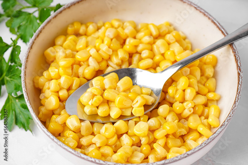 Bowl with canned corn, spoon and parsley on white table