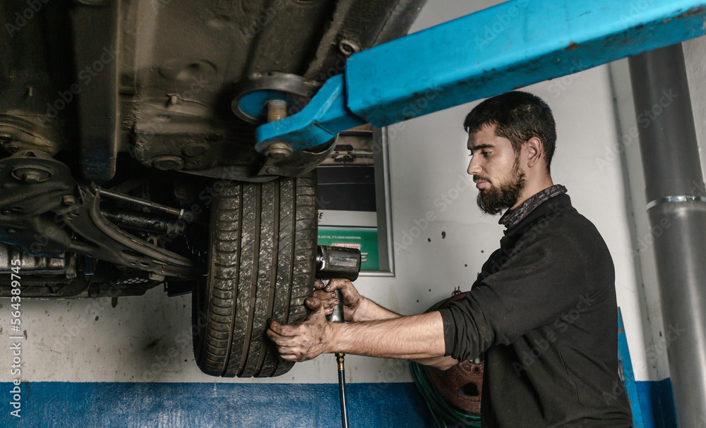 Bearded mechanic with screwdriver repairing car wheel in workshop