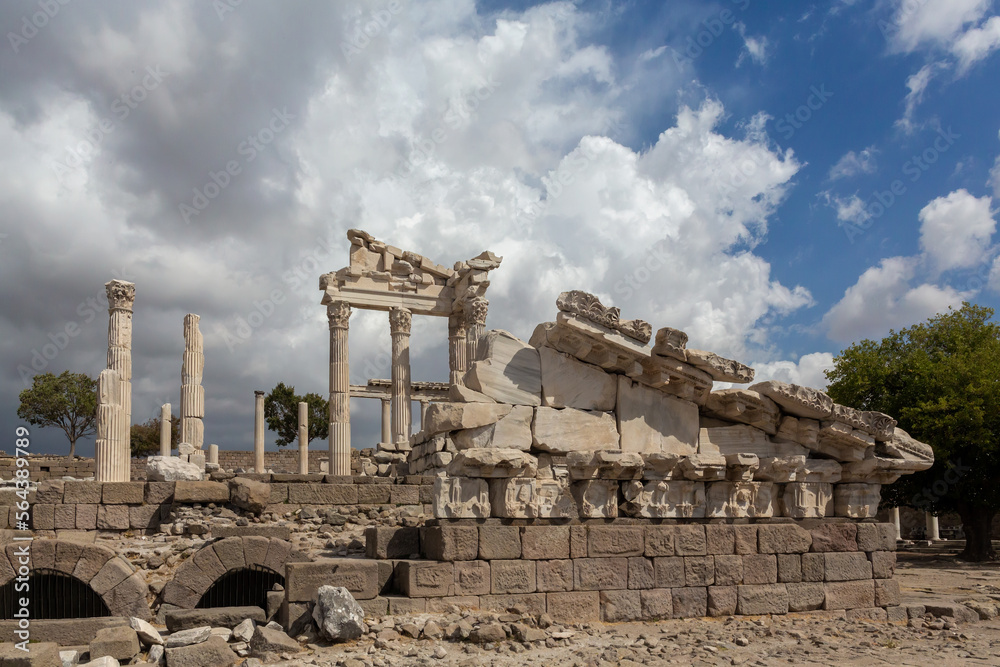 Ruined Temple of Trajan in Pergamon Ancient City. Fragment of fronton and columns with ccorinthian capitals. Dramatic sky at background. History, art or architecture concept. Bergama, Turkey (Turkiye)