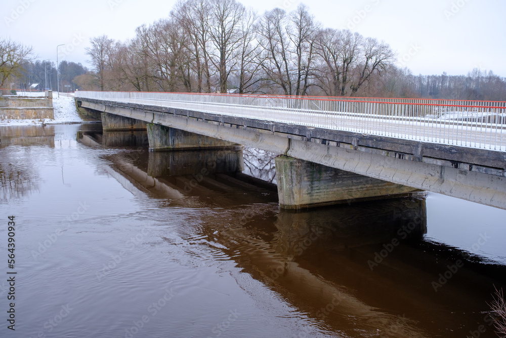 River Aiviekste in Vidzeme, Latvia in winter time. High water level in the river, dark January day. Bridge over the river