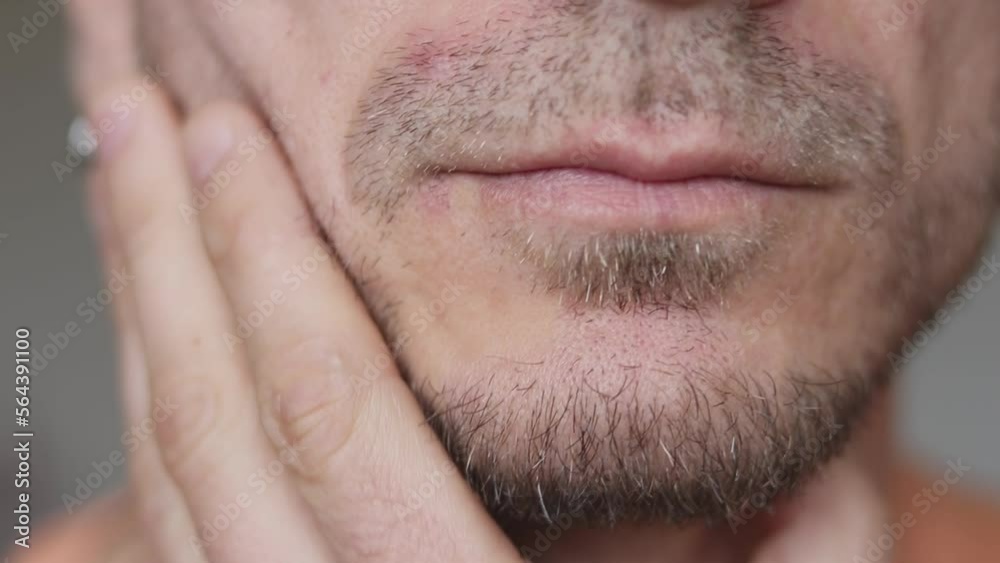 Close-up of a man's stubble. A young man is touching the beard stubble on his face with his hand. Unshaven male beard with black stubble. Hair on a man's skin. Close-up of a man's stubble. A young man is touching the beard stubble on his face with his hand. Unshaven male beard with black stubble. Hair on a man's skin.
