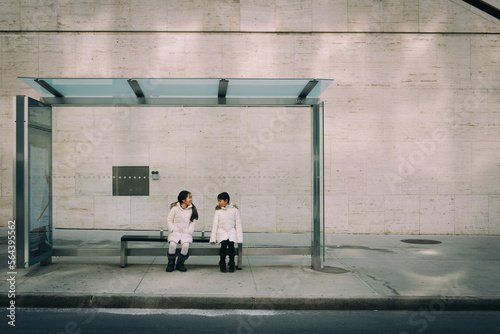Two asian girls dressed in winter clothe sitting at a bus stop in the city