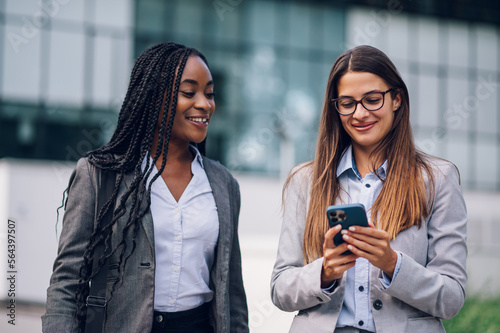 Two multiracial business woman meeting outside and using a smartphone