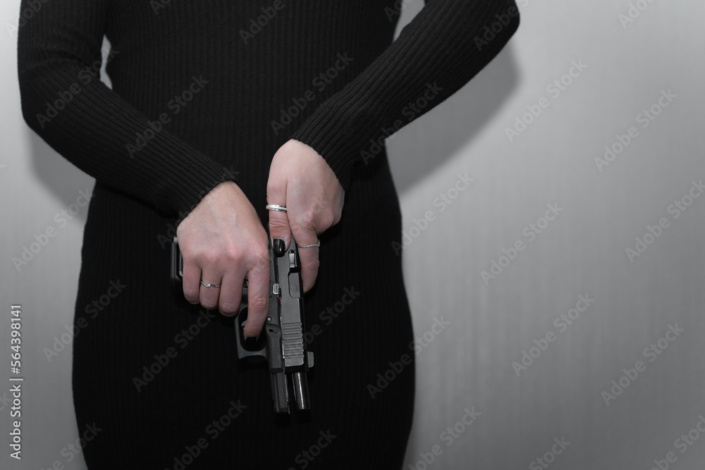 A pistol in female hands, a girl in a black dress has a firearm.