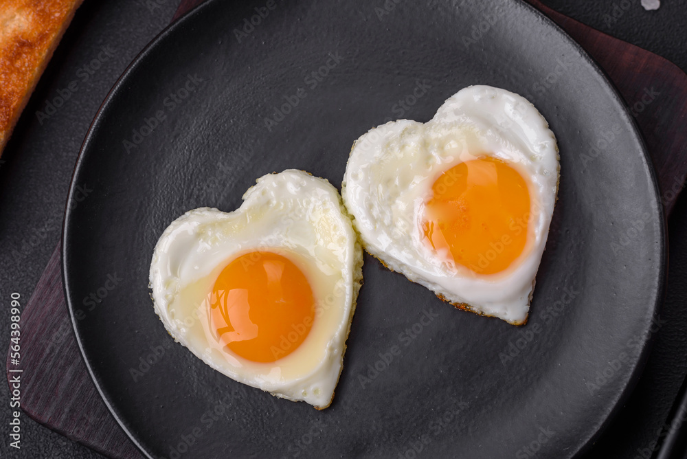 Two heart-shaped fried eggs on a black ceramic plate on a dark concrete background Two heart-shaped fried eggs on a black ceramic plate on a dark concrete background