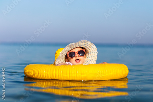 Foto Cute little girl in ocean with swimming float, wearing sunglasses and sunhat