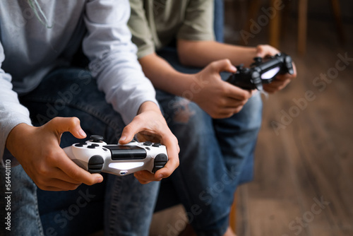 kids hands with joysticks, two children siblings playing video game console while sitting at home, real people, leisure concept.