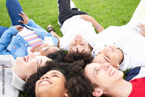 Group of happy teenagers friends having fun together outdoors. Smiling multiracial young people enjoying lying on the grass in the park. High quality photo