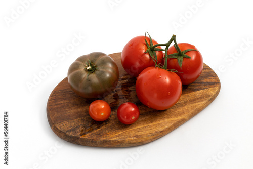 Black tomatoes and cherry tomatoes on wooden chopping board on white background isolated