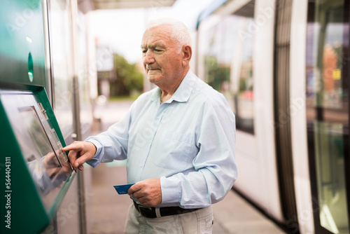 Εκτύπωση καμβά Elderly Caucasian man using cash machine to withdraw his money while standing on tram station