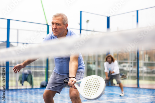 Portrait of elderly man playing paddle tennis with friends on open court. Active lifestyle concept