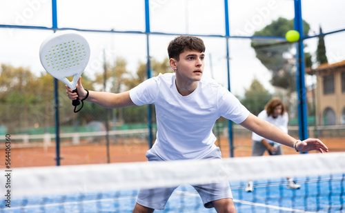 Focused young man playing paddle tennis couple match at outdoors court