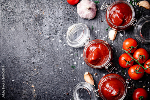 Tomato sauce in glass jars on a stone board with spices. 