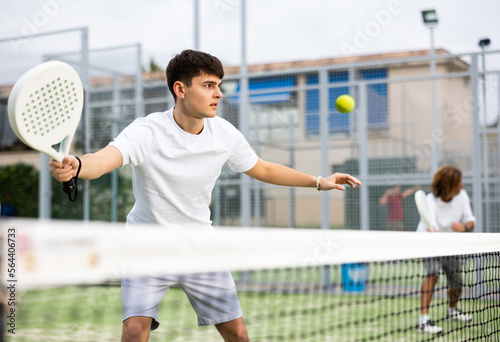 Sportive young man playing padel together with a partner. View through the tennis net © JackF