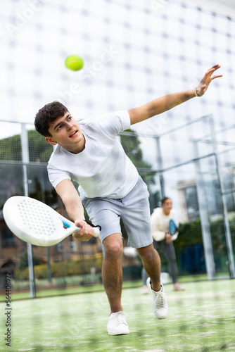 Sportive young man playing padel with partner on tennis cort in spring. View through tennis net