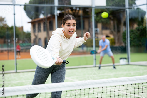 Cheerful fit young girl paddle tennis player waiting to receive serve, ready to perform forehand to return ball to opponent field on outdoor court on summer day © JackF