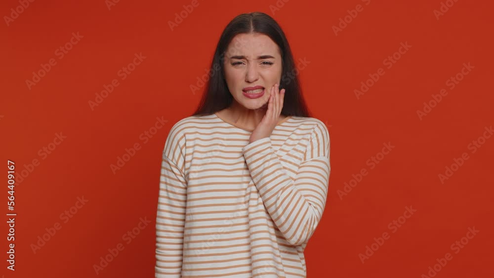 Hipster pretty woman touching sore cheek suffering from toothache cavities or gingivitis waiting for dentist appointment gums disease. Young girl indoor studio shot isolated alone on red background Hipster pretty woman touching sore cheek suffering from toothache cavities or gingivitis waiting for dentist appointment gums disease. Young girl indoor studio shot isolated alone on red background