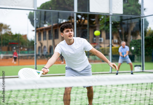 Portrait of young sporty guy playing paddle tennis with friends on open court. Active lifestyle concept © JackF