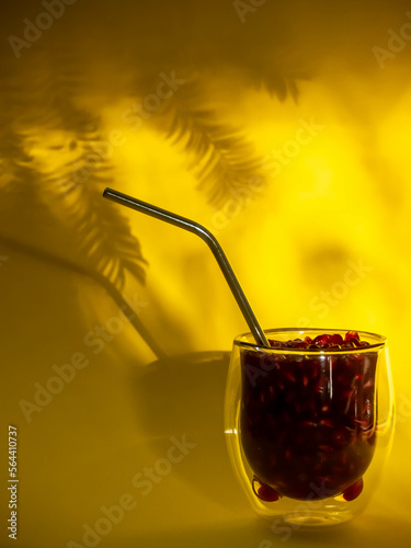 Glass beaker with pomegranate on a yellow background.