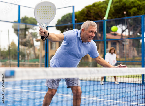 European old man holding padel racquet in hand and ready to return ball while playing in court