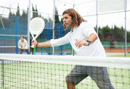 Portrait of focused adult man playing paddle tennis couple match at outdoors court © JackF