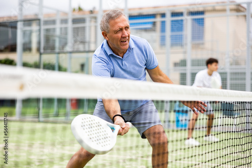 Portrait of elderly man playing paddle tennis with friends on open court. Active lifestyle concept © JackF