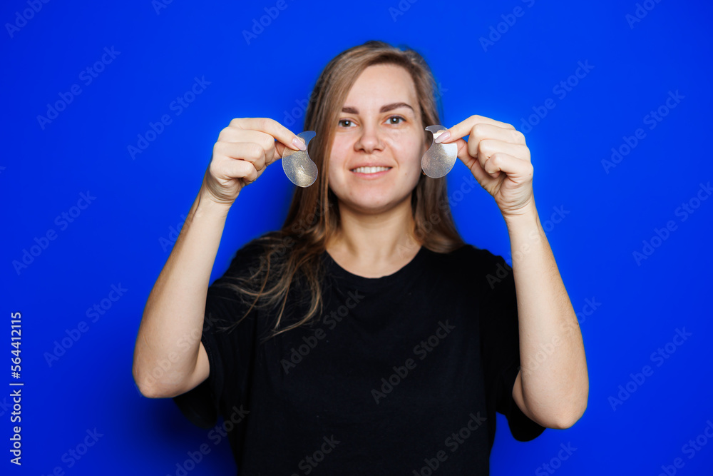 Cute young blonde woman with natural smooth skin without makeup posing happy and smiling at camera while standing in t-shirt on blue background. Beauty concept, eye patches for women Cute young blonde woman with natural smooth skin without makeup posing happy and smiling at camera while standing in t-shirt on blue background. Beauty concept, eye patches for women