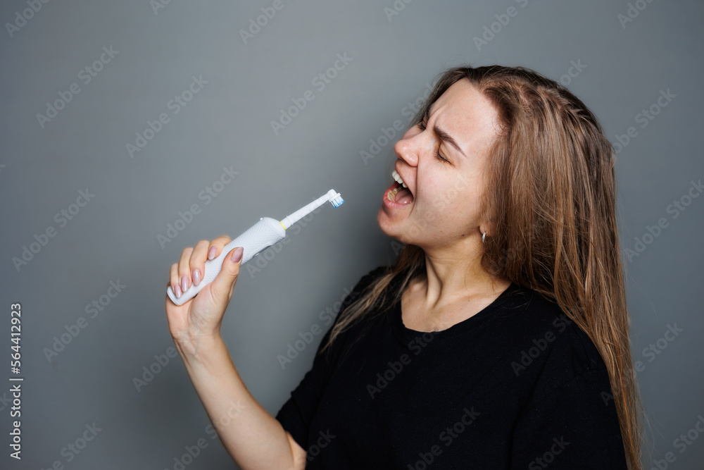 Obraz premium Portrait of a smiling young woman without makeup in a black t-shirt brushing her teeth, mature woman, natural beauty concept. Morning brush for teeth, dental ultrasonic brush.