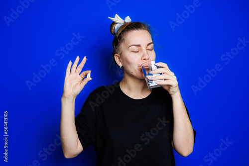 Smiling young woman without makeup in black t-shirt drinking vitamins for health, mature woman, natural beauty concept. Morning glass of water, immune care, vitamin complex for women. Selective focus