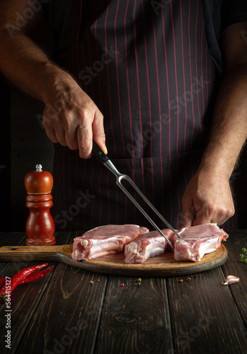 Professional chef cooking lunch with raw sliced meat steaks on the cutting board of the restaurant kitchen. Delicious grill idea. Copy space