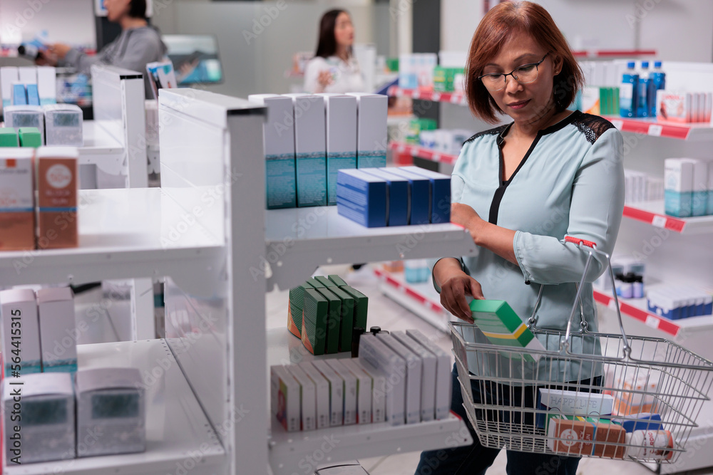 Asian woman examining vitamins box on shelves, looking to buy medical supplements and pharmaceutical products. Checking package of healthcare supplies and medicaments in pharmacy shop.