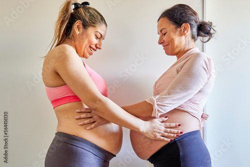 Happy pregnant women toching each others bellies. Multiethnic couple sorority photo