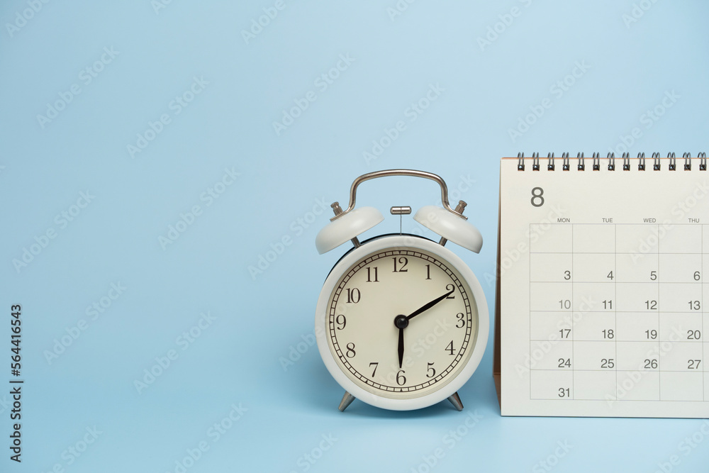 Naklejka premium close up of calendar and alarm clock on the blue table background, planning for business meeting or travel planning concept