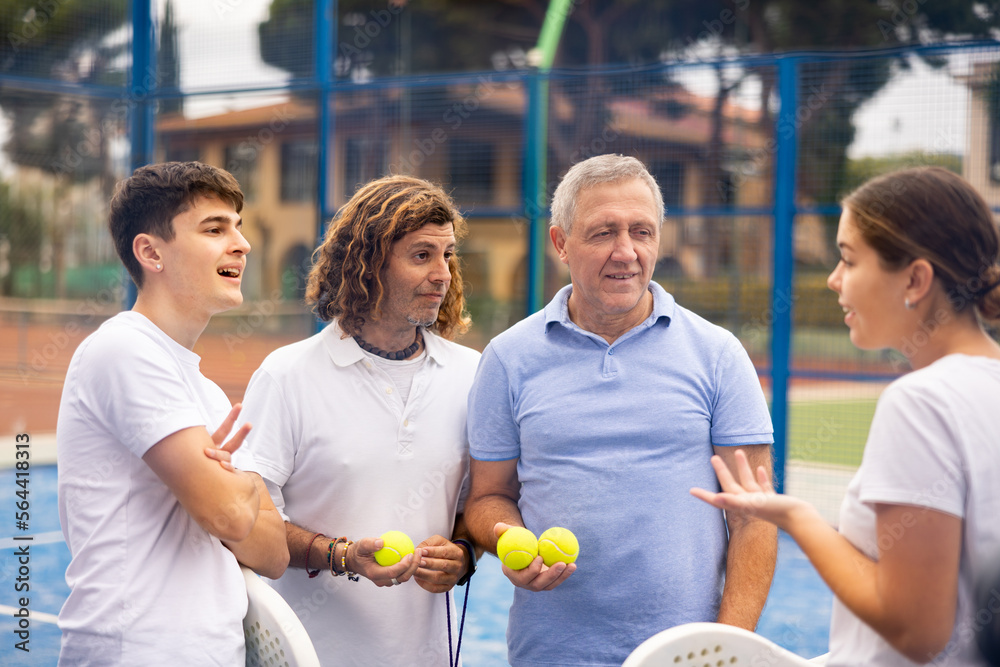 Fototapeta premium Two pairs of padel players are happily discussing the past game on an open court
