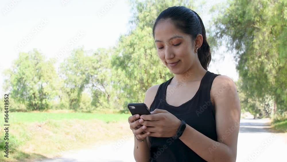 Video de una mujer joven caucasica delgada con ropa de deporte en la naturaleza texteando con su telefono inteligente 