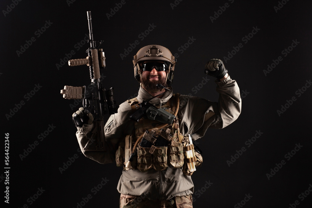 USA soldier in a military suit with a rifle smiles and shows strength against a dark background, an American commando in uniform