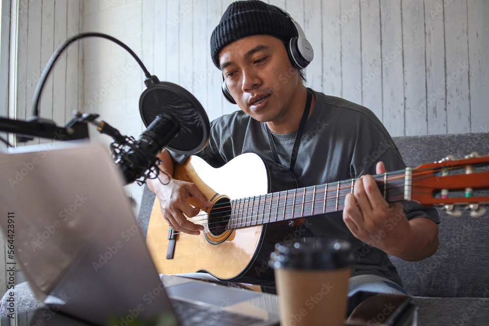 Obraz premium Asian influencer playing guitar during podcast or live video broadcast at home studio
