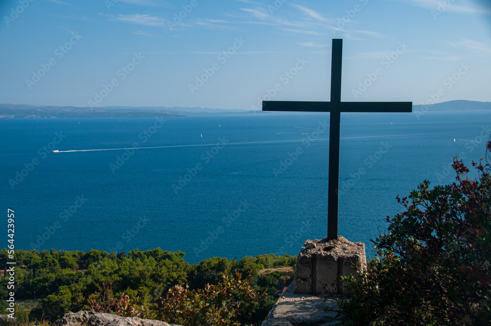 A religious cross at the top of the hill has boats go by on the Mediterranean Sea