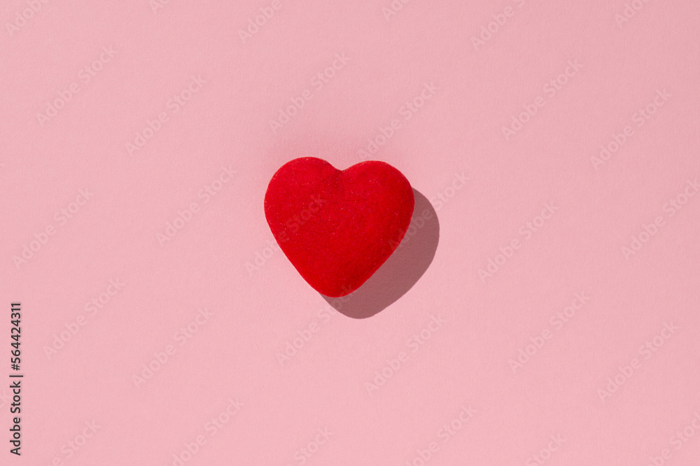 Red heart on a pink background under hard lighting.View from above.