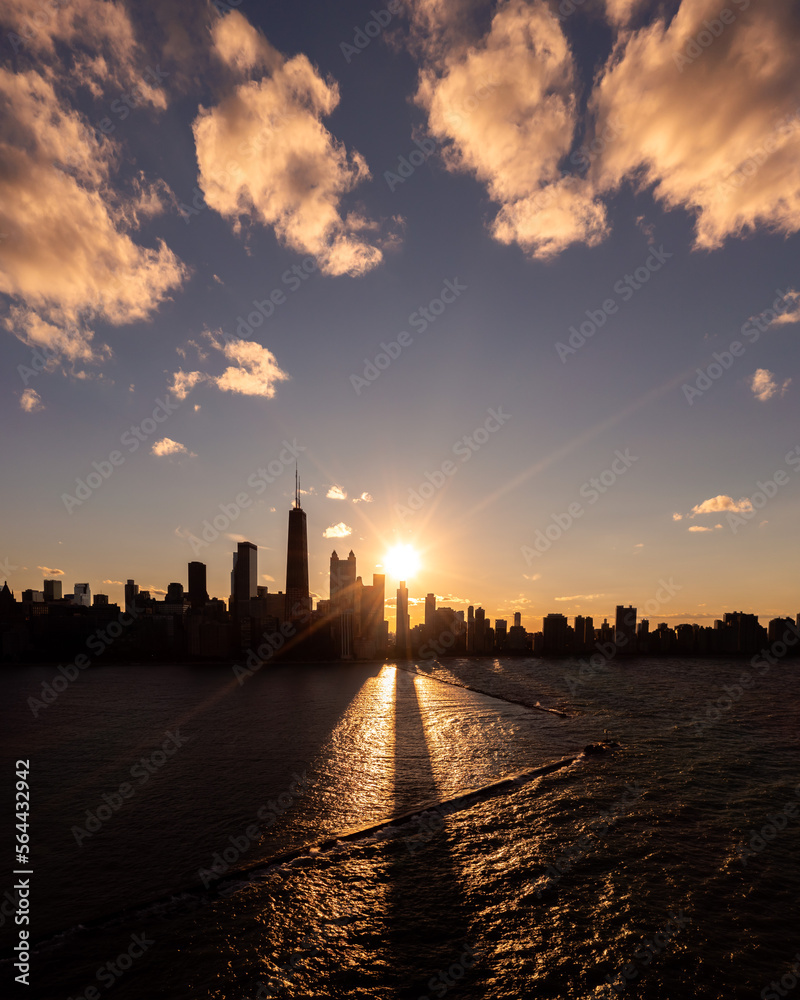 Beautiful downtown Chicago skyline aerial drone photograph above Lake Michigan during the  autumn equinox sunset as the sun casts a glistening yellow glow and long building shadows over the water.